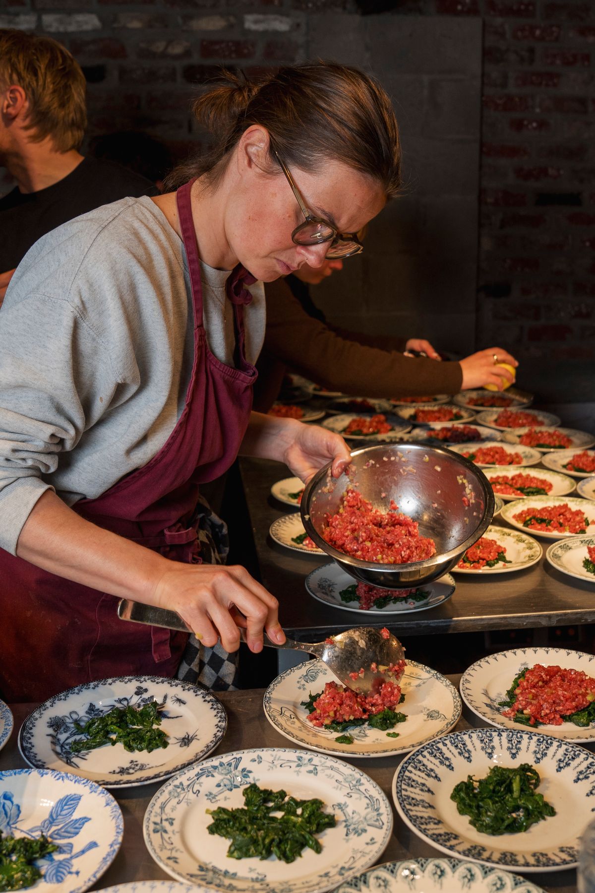 Chef Margaux Tataer is volop bezig met het dresseren van de rundstartaar met Jersey Blue, ondersteund door Géry Van Peteghem van Kartouche.